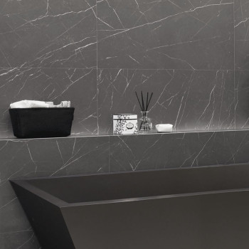 An grauen Marmorwänden steht eine schwarze rechteckige Badewanne. Darüber befindet sich auf einem Regal ein Korb mit Handtüchern