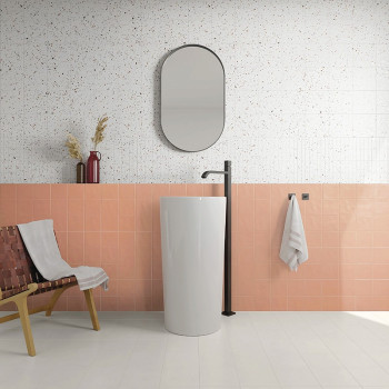 Een hoge, witte cilindrische wastafel staat met een zwarte kraan in een badkamer versierd met roze en gespikkelde tegels, naast 