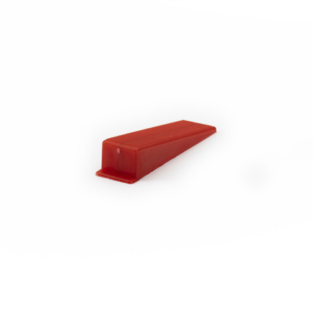 A red, wedge-shaped doorstop lies on a plain white surface, angled slightly upwards, with no visible text or markings.
