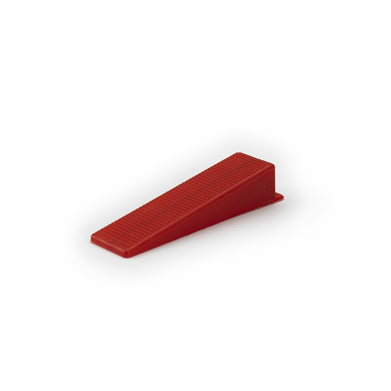 Un petit coin en plastique rouge à texture striée se trouve sur un fond blanc uni.