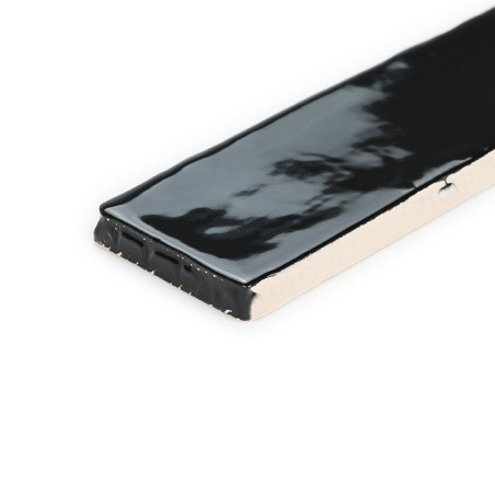 A rectangular ceramic tile is partially shown, featuring a glossy black glaze on its surface, set against a plain white backgrou