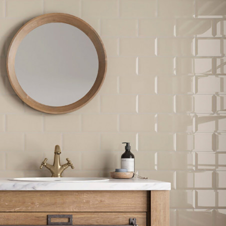 Ronde spiegel hangt boven een beige tegelwand. Houten wastafel ondersteunt een marmeren gootsteen met koperen kraan en een zeepd