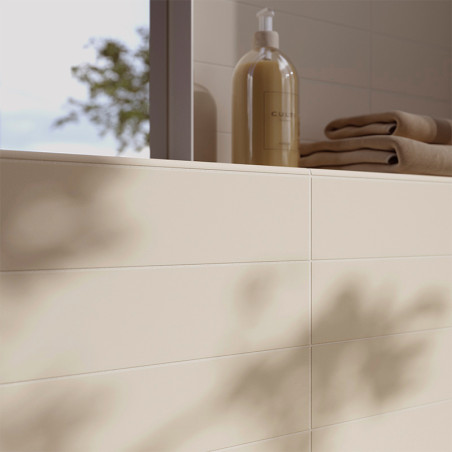 Los azulejos de color crema se alinean en la pared del baño y proyectan sombras suaves. Cerca de allí, sobre una repisa, hay un 