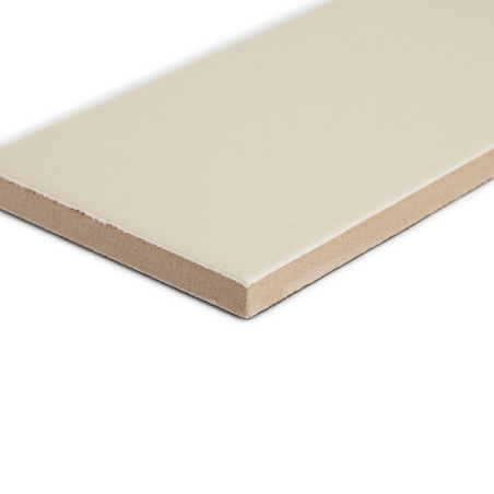 Un carreau de céramique rectangulaire beige repose à plat sur une surface blanche, présentant un dessus lisse et un bord inachev
