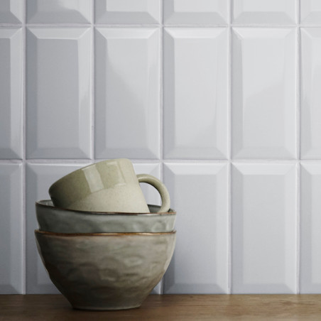 A stack of ceramic bowls and a mug sits on a wooden surface, in front of glossy, geometric-patterned white wall tiles.