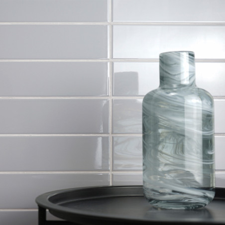 Eine gewirbelte Glasflasche ruht auf einem schwarzen Tablett vor einer glänzend weißen U-Bahn-Fliesenwand und reflektiert das Um