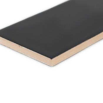Un carreau de céramique rectangulaire, présentant une surface noire lisse et un dessous beige, repose sur un fond blanc uni.