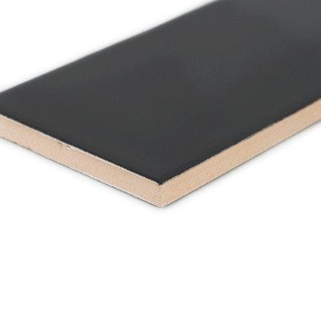 Un carreau de céramique rectangulaire, présentant une surface noire lisse et un dessous beige, repose sur un fond blanc uni.