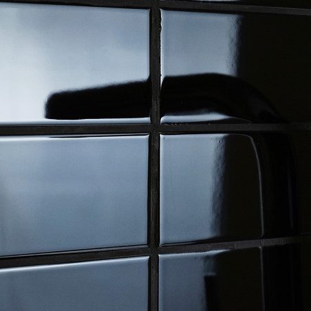 Black, glossy ceramic tiles reflecting light form a grid pattern. A shadow curves across one tile, suggesting a nearby object or