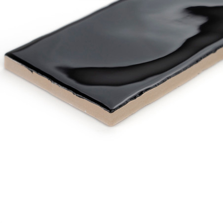 Un azulejo cerámico rectangular presenta una superficie negra brillante, que muestra ligeras ondulaciones, sobre un fondo blanco