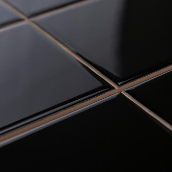 Glossy black tiles arranged in a grid pattern, reflecting light, with tan-colored grout, creating a sleek and modern surface.