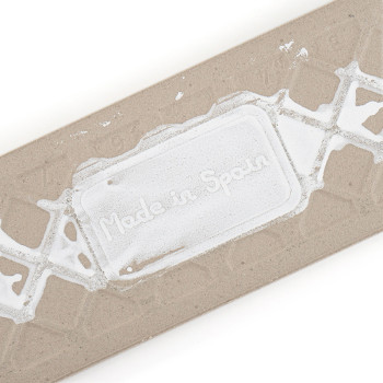 Een rechthoekige beige tegel is voorzien van de tekst `Made in Spain` in reliëf in een wit geometrisch patroon, waardoor de oors