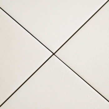 Quatre carreaux de céramique blanche se rejoignent en un point central, formant une forme en plus avec des lignes de coulis étro