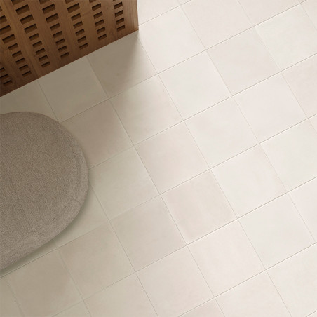 Un sol carrelé beige clair s'étend sur toute la pièce. Un pouf rond en tissu beige repose dans un coin à côté d'un panneau en bo