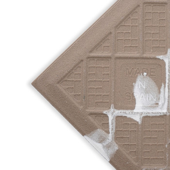 A brown tile features a textured grid pattern with white paint splashes, inscribed with `MADE IN SPAIN,` situated against a whit