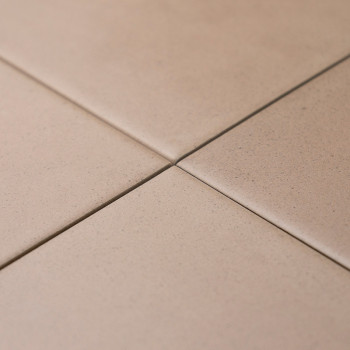 Vier beige tegels kruisen elkaar netjes en vormen op de hoeken een klein kruis. Ze bevinden zich op een vlak, effen oppervlak.