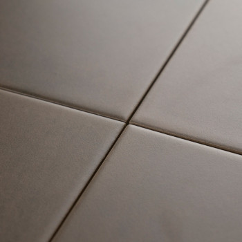 Four smooth, matte, square tiles meet at a central grout line, forming a minimal grid pattern against a neutral-toned surface.