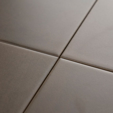 Four smooth, matte, square tiles meet at a central grout line, forming a minimal grid pattern against a neutral-toned surface.