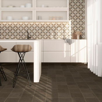 Voor witte kasten staat een keukeneiland met twee houten barkrukken. Achterwand van mozaïektegels siert de muur. Zonlicht stroom