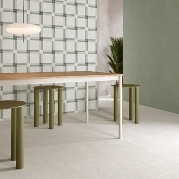 Une table de salle à manger moderne repose sur des carreaux carrés clairs, entourée de tabourets cylindriques verts. Un mur et u