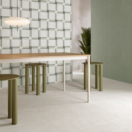 A modern dining room table sits on light square tiles, surrounded by green cylindrical stools. A plaid-patterned wall and plant 