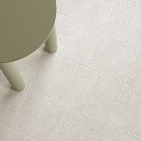 Un pied de table rond vert olive repose sur une grille de carreaux beige clair, créant un aspect de sol moderne et minimaliste.