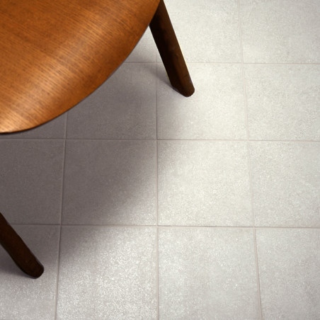 Une table ronde en bois recouvre partiellement une grille de carrelage gris clair, créant un décor intérieur chaleureux et minim