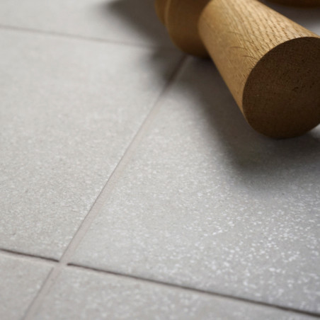 Um rolo de massa de madeira repousa sobre uma superfície lisa de azulejos cinza claro, criando um ambiente de cozinha simples e 