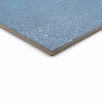 Un carreau de céramique bleu, posé à plat, présente une texture mouchetée sur sa surface lisse sur un fond blanc uni.