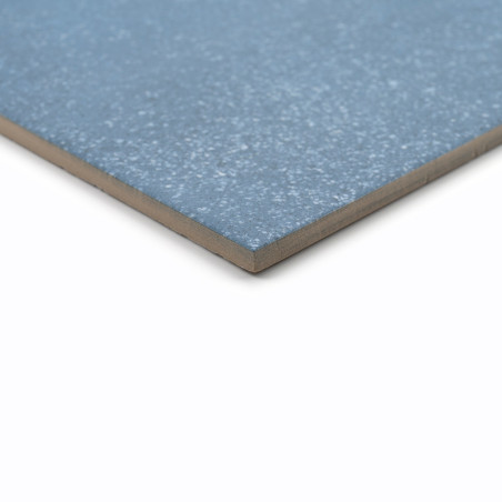 Un carreau de céramique bleu, posé à plat, présente une texture mouchetée sur sa surface lisse sur un fond blanc uni.