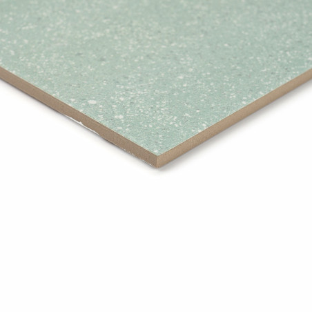 Um ladrilho cerâmico salpicado de verde assenta sobre um fundo branco, mostrando sua superfície lisa e polida e bordas angulares