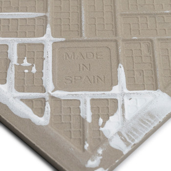 Op een beige getextureerde tegel staan ​​in het midden de woorden `MADE IN SPAIN`. Langs de rasterpatronen verschijnen witte lij
