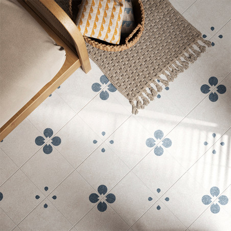 A light gray floor tile features blue floral motifs, creating a symmetrical pattern. Its adjacent to a wicker chair and fringed 