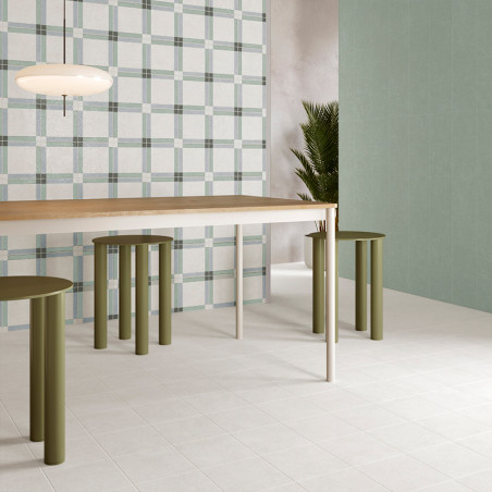 Una habitación minimalista cuenta con una mesa de madera con taburetes cilíndricos verdes debajo. Una pared con estampado de cua