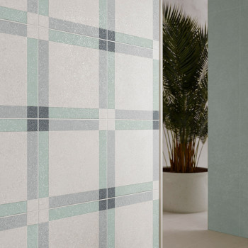 Una pared de azulejos muestra un patrón de cuadros en gris suave, verde y azul, colocado en el interior junto a una palmera en m