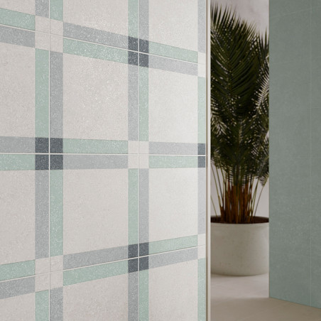 Una pared de azulejos muestra un patrón de cuadros en gris suave, verde y azul, colocado en el interior junto a una palmera en m