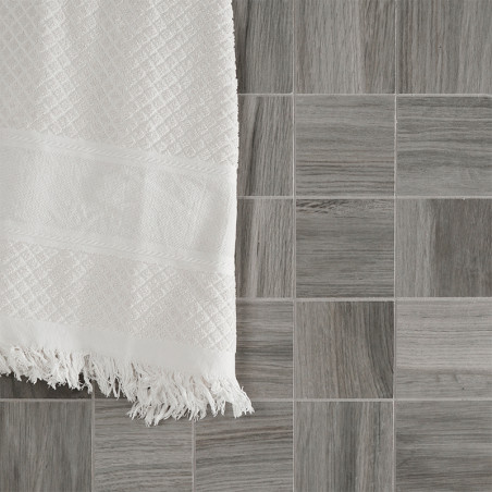 Une serviette blanche et texturée est suspendue sur une grille de petits carreaux gris carrés avec un motif imitant le bois, cré