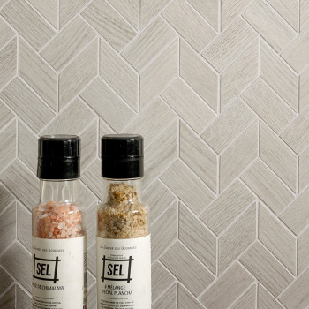 Duas garrafas de especiarias estão encostadas em uma parede de azulejos cinza claro em espinha. O texto nas garrafas diz `SEL,` 