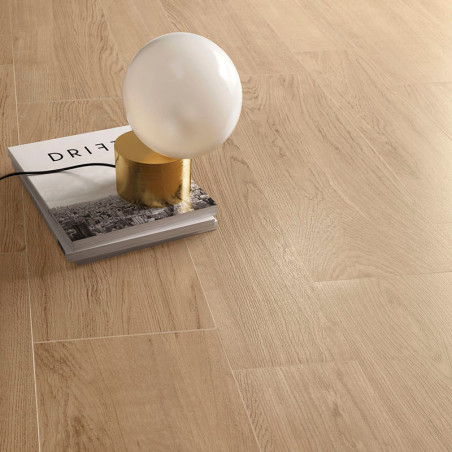 Una lámpara esférica descansa sobre un libro titulado `DRIFT`, colocado sobre un piso de madera clara, creando un ambiente minim