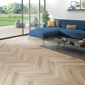 Des carreaux beiges à chevrons recouvrent le sol du salon, menant à de grandes portes vitrées. Un canapé sectionnel bleu et une 