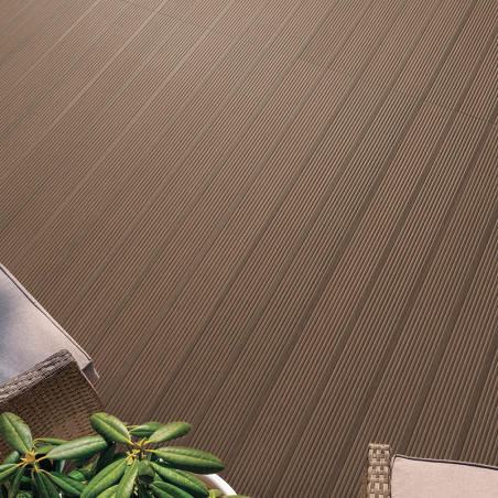 Des carreaux marron avec des rainures parallèles se trouvent à l'extérieur, à côté d'une chaise en osier et d'une plante verte, 