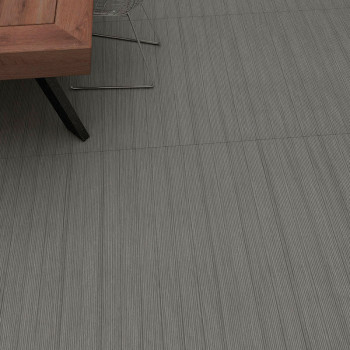 Un pied de table en bois repose sur des carreaux gris texturés avec des lignes verticales subtiles, installés dans un décor inté