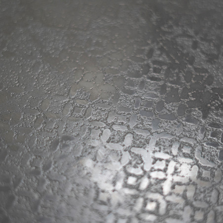 A textured, frosted glass surface features an intricate, repeating geometric pattern, reflecting light softly in a neutral gray 