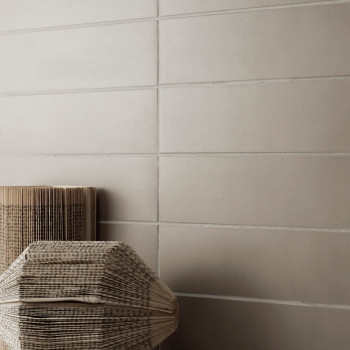Neutraal beige tegels vormen een gladde, horizontaal opgestelde muur, waar gevouwen papieren lantaarns tegenaan rusten, waardoor