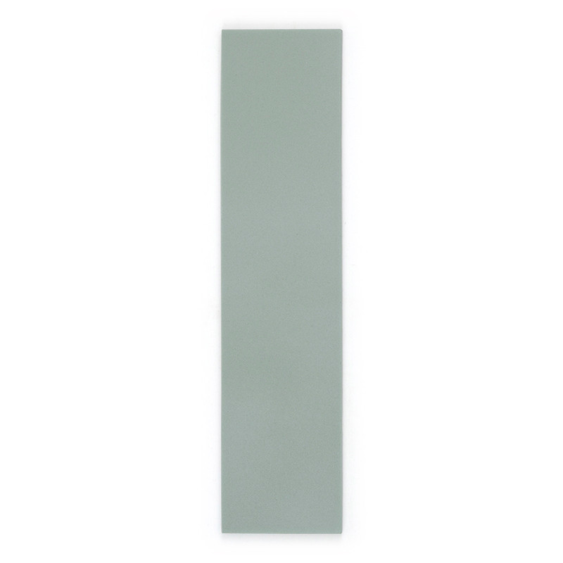 Un azulejo largo, rectangular y de color verde claro se alza sobre un fondo blanco liso, resaltando la textura de su superficie 
