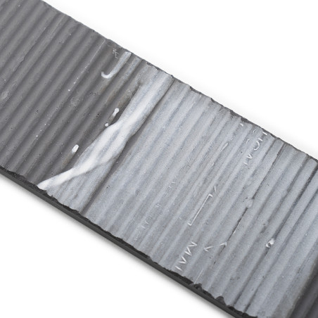 Un azulejo rectangular acanalado muestra un degradado de gris oscuro a claro con ranuras texturizadas. Se ven rayas blancas y un