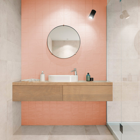 Een ronde spiegel hangt boven een houten wastafel met wastafel en toiletartikelen tegen een roze betegelde muur in een moderne b