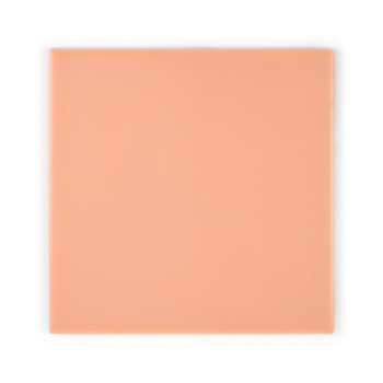 Un carreau de céramique lisse de couleur pêche repose sur un fond blanc uni. Le carreau est carré avec une finition brillante et