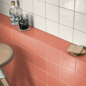 Flessen en glazen rusten op koraalkleurige en wit betegelde oppervlakken in een keukenomgeving, met onderzetters ernaast op een 