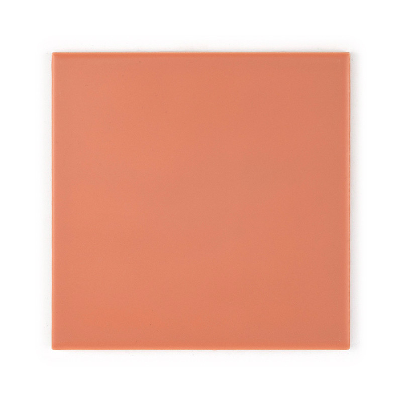 Un carreau de céramique lisse et carré de couleur pêche, reposant sur une surface plane de couleur claire, avec une subtile fini